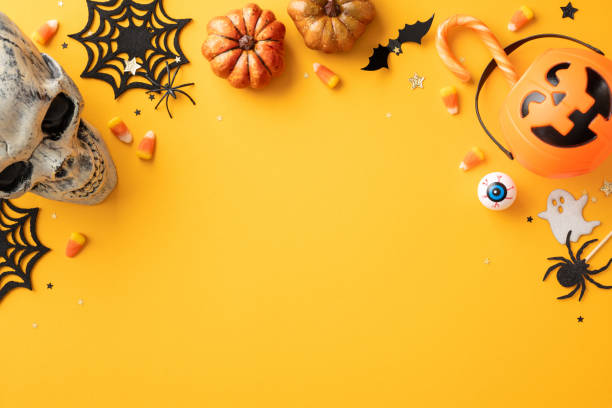 istock Halloween-themed background with a skull, pumpkins, candy corn, spider webs, and various spooky decorations arranged on an orange surface 2165250028
