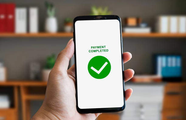 istock hand holding smartphone with payment completed notification checkmark sign on screen on indoor room background 2165259118