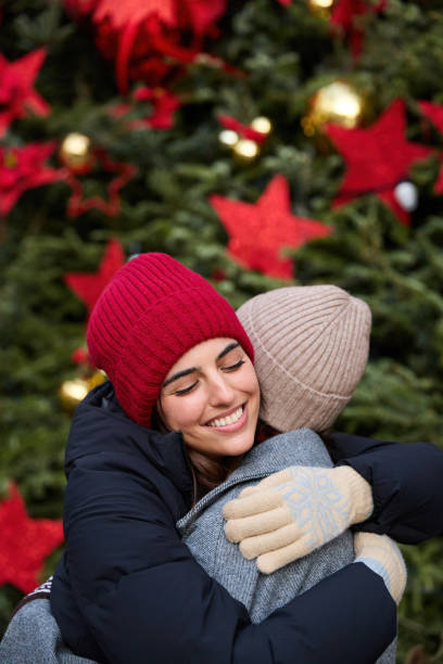 istock Two happy friends embracing in front of christmas tree 2165278097