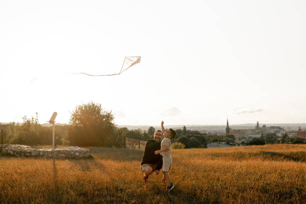 In this joyful image, a father and his little boy share a moment of pure delight while playing with a kite outdoors.