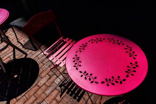 Looking down on an outdoor cafe's pink metal table and chair on a city sidewalk at night.