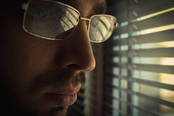 istock A Caucasian man with a beard and mustache and glasses stands at a window with blinds 2165292913