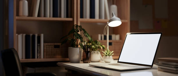 istock A laptop computer mockup on a table in a dark room at night, illuminated by a table lamp. 2165302393