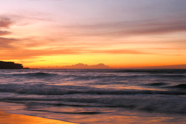 Waves crashing at sunrise on Bondi Beach. On the left is Ben Buckler headland. The silhouettes of Godzilla and King Kong can be imagined in the rock face. This image was achieved with a 1/2 second exposure and taken on a cold and sunny morning before sunrise on 4 August 2024.