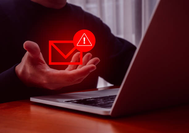 istock Scammer attack with sms spam phishing online communication concept. Red envelope with warning icon in hacker's hand who use laptop computer cyberattack sending scam malware spreading virus email. 2165305110