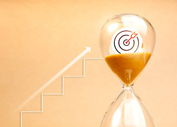 istock Short-term business goals encompass work that helps an organization reach its mid-term goals, steps to success concept. Arrow rise on stairway up to big target icon in hourglass on yellow background. 2165305119