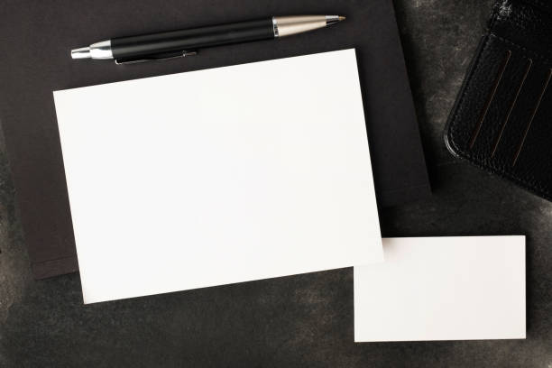 Blank white greeting card or invitation with notebook and pen on black background. Mockup presentation. Flat lay. Top view with copy space. Modern minimalist style.