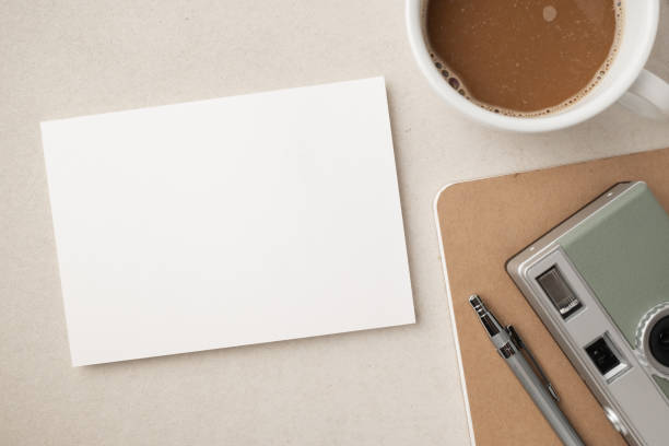 istock Blank white greeting card or invitation with coffee cup, camera, notebook and pencil on beige background. Mockup presentation. Flat lay. 2165308113