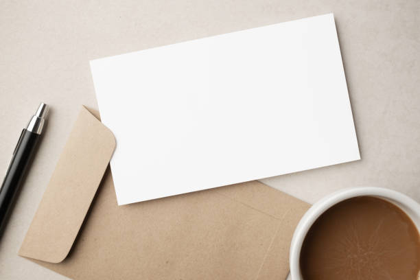 istock White blank greeting or invitation card and envelope with coffee cup, notebook and pencil on beige background. Mockup presentation. Flat lay. 2165308137