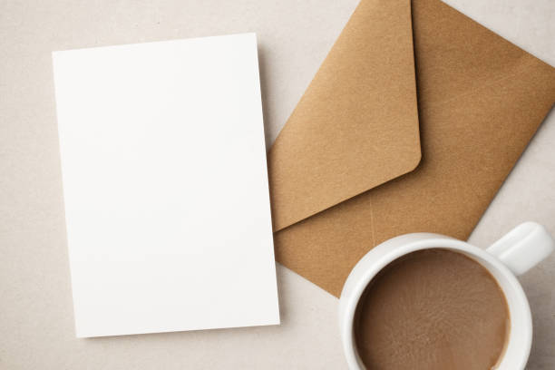 istock White blank greeting or invitation card and envelope with coffee cup, notebook and pencil on beige background. Mockup presentation. Flat lay. 2165308148