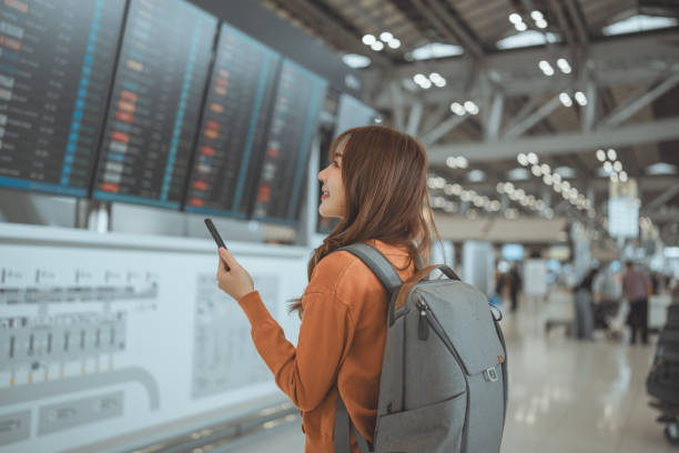 istock Happy asian woman traveller using mobile smartphone and checking flight at the flight information board, Tourist journey trip concept. 2165314796