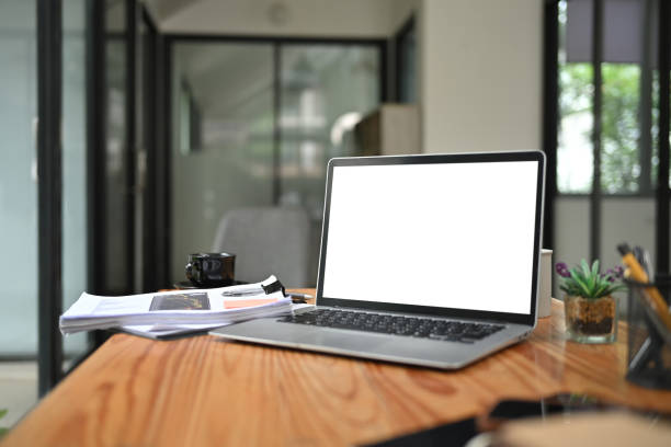 istock Laptop computer with white blank screen and office supplies on wooden table 2165315327