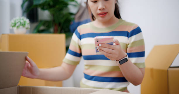 istock Young woman putting things in boxes and using a mobile phone. 2165317140