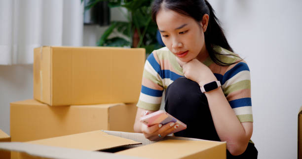 istock Young woman putting things in boxes and using a mobile phone. 2165317172