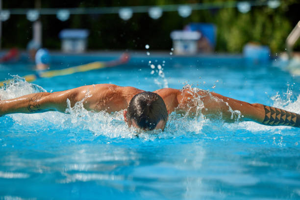 Woman swimmer in goggles and cap executes butterfly stroke in an indoor pool during a race.