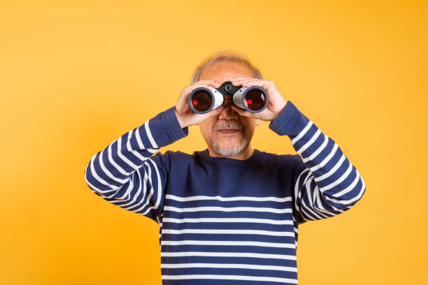 istock Portrait Asian smiling old man looking camera through binoculars studio shot isolated yellow background, senior man pensioner feeling surprised 2165322301