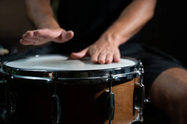 A drummer's hand strikes a snare drum, creating a sharp and distinct sound. The drum is wooden with chrome hardware, and the hand is well-defined. stock photo