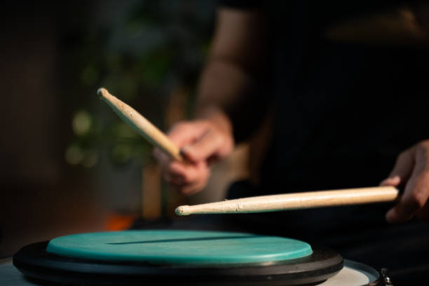 istock A person plays drumsticks on a green practice pad while sitting in a dimly lit studio. The pad is on top of a drum and the person is wearing a black shirt. 2165322848