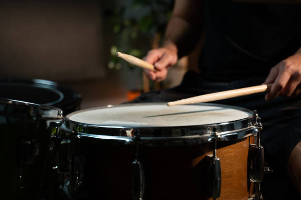 istock A drummer plays a snare drum in a dimly lit studio setting. The drummer is wearing a black shirt and uses a wooden drumstick to play the drum. The snare drum is a standard size, wooden drum with chrome hardware. 2165322868