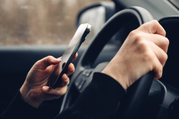 istock Closeup of female hands typing text message on cell phone while driving car through countryside landscape in winter 2165328001