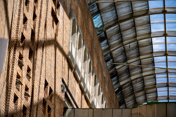 An upward-looking photo taken inside the Xinjiang International Grand Bazaar, showcasing the distinctive architectural facade and the translucent skylight dome above. Sunlight beautifully illuminates the building's facade, enhancing its striking design and creating a visually stunning effect.