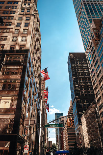 New York, USA - July 25 2024: Tall modern buildings with American flags in downtown New York, Manhattan against blue sky