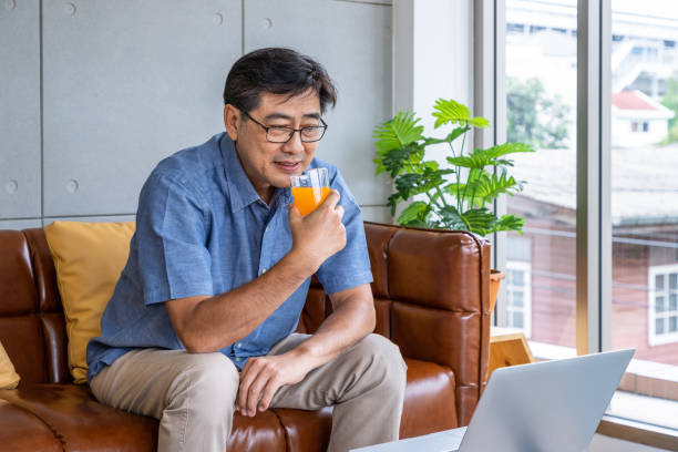 istock Senior Asian man drinking orange juice while working on laptop at home 2165340582