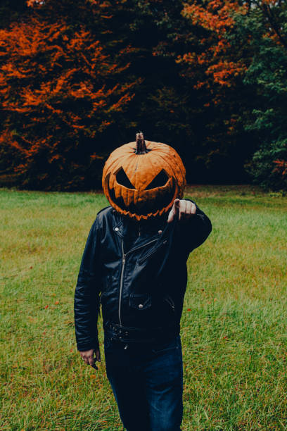 istock Man wearing black leather jacket and a jack o lantern costume pointing a finger at a camera. Concept of halloween spirit 2165341221