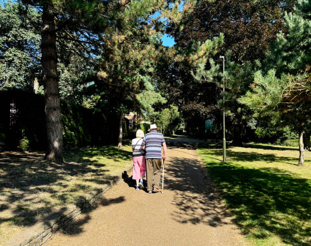 Two pensioners walking together in Waterloo Park in Norwich on a sunny summer morning. August 2024