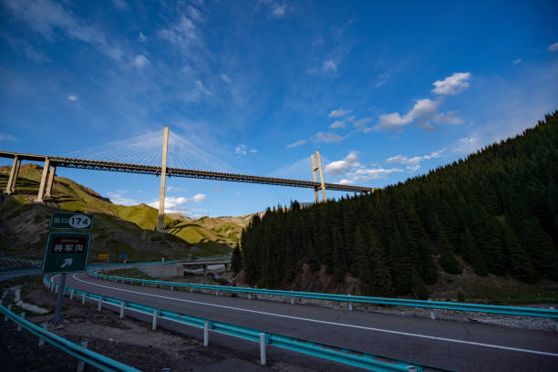 A photo of Guozi Gorge Bridge on the highway in Xinjiang, illuminated by sunlight. The background features a clear blue sky. Guozi Gorge Bridge, part of National Highway 045 connecting Sayram Lake to Guozi Gorge, is a cable-stayed bridge with a total length of approximately 700 meters and a clearance of about 200 meters above the valley floor. It represents a significant advancement in Xinjiang's highway construction with its integration of new technology, structures, processes, and equipment.