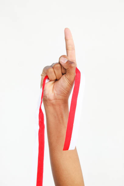 A man with a fist holding a red and white ribbon with empty copy space isolated on a white background, representing Indonesia Independence Day concept. celebrating Indonesia's Independence Day