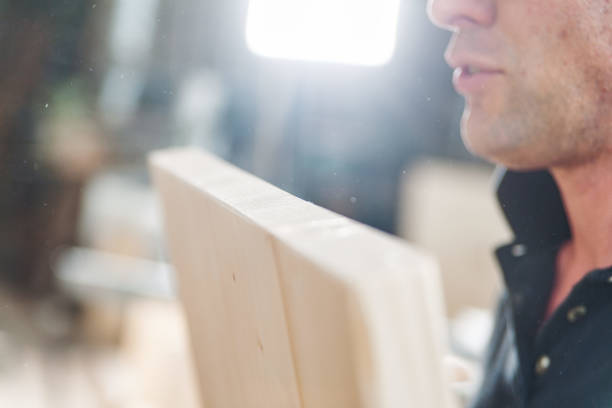 Carpenter is analyzing a wood plank in a workshop, with sawdust particles visible in the air, highlighting the craftsmanship involved