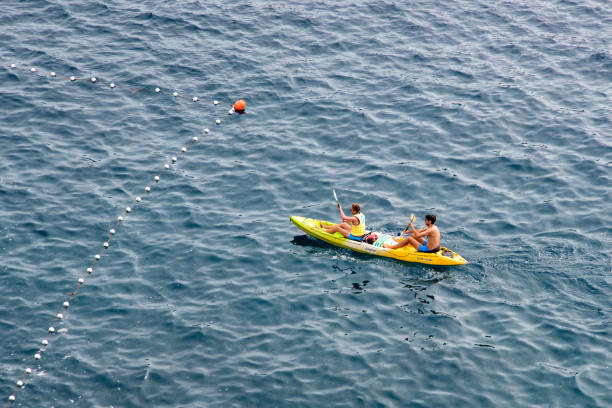 An individual paddling a vibrant orange kayak across a serene blue river, viewed from above. The water ripples gently around the kayak, emphasizing tranquility and outdoor adventure.