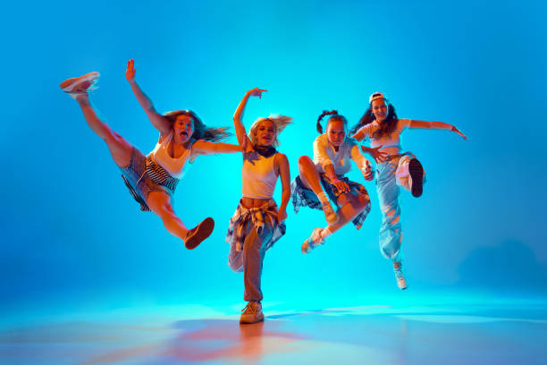 istock Four dancers leap into air with exuberant and dynamic poses in vibrant neon light against gradient studio background. 2165378381