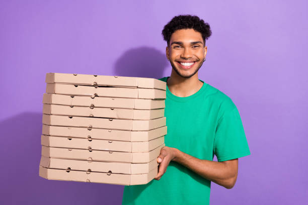 istock Photo of attractive funky guy dressed green t-shirt delivering pizza boxes pile stack isolated violet color background 2165383263
