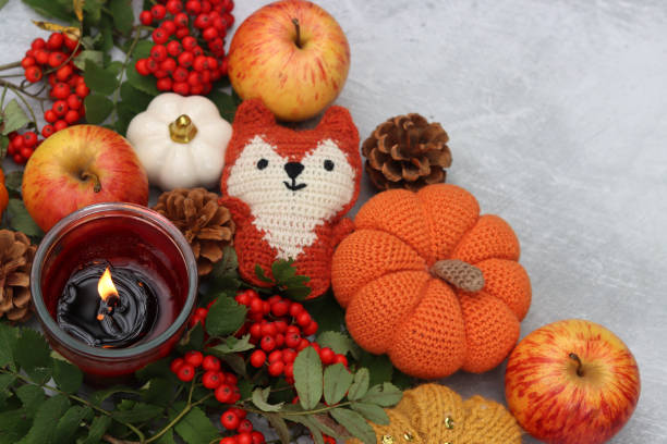 Handmade fox toy, pumpkins, apples, rowan berries and a candle on a light background with space for text. Autumn decorations close up photo.