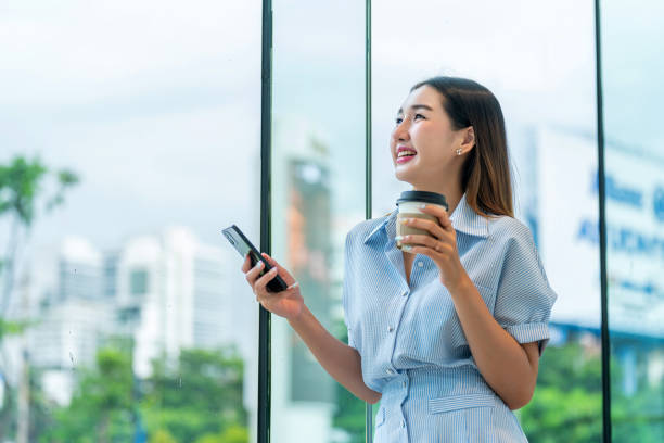 istock Young Woman Using Phone While Having A Cup of Coffee, Looking Away 2165387616