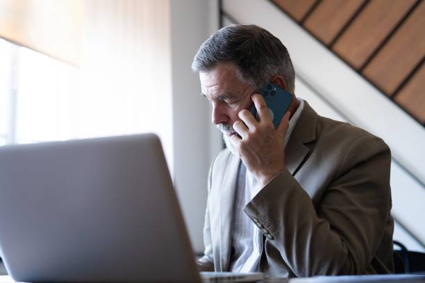 istock Middle aged businessman making call on cellphone using laptop in office 2165389852