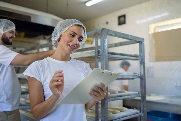 istock Woman in bakery checking a list on clipboard smiling 2165392399