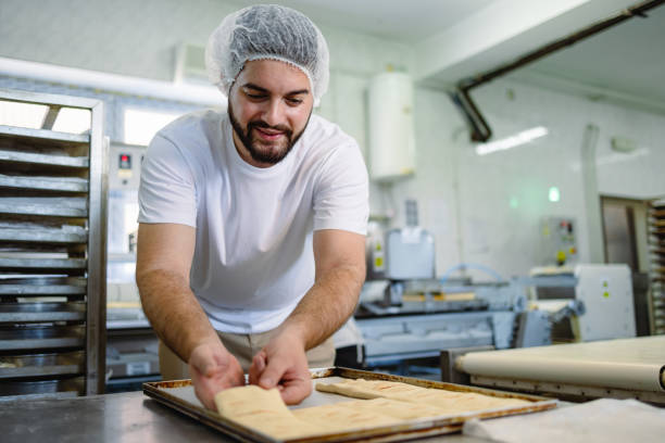 istock Male baker rolling dough on a tray in bakery kitchen. 2165392587