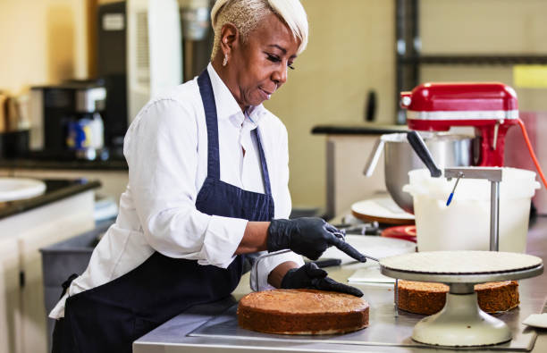 istock Senior black woman making cake in bakery, cutting layers 2165396687