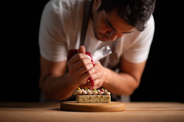 istock A male pastry chef squeezing strawberry sauce from icing bag to a cake 2165399300
