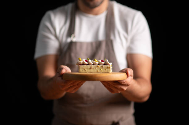 A male pastry chef holding a cake with pistachios and strawberry on dark background.