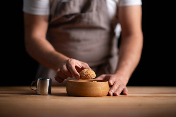 A male pastry chef preparing profiteroles on a wooden table and dark background.