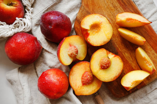 Ripe cut peaches on a wooden board and a linen napkin next to a string bag