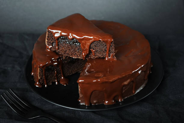 istock Chocolate cake with chocolate icing on a black plate next to a fork 2165404400
