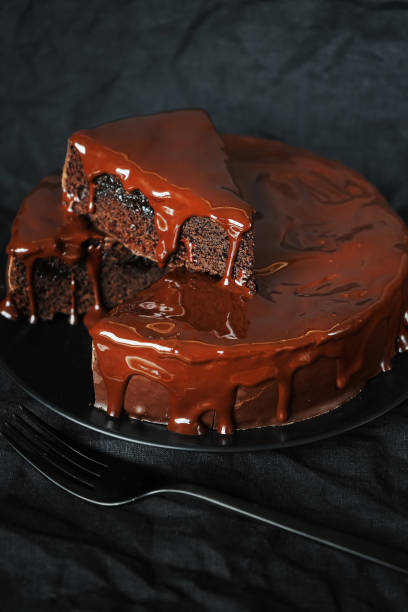 istock Chocolate cake with chocolate icing on a black plate next to a fork 2165404406