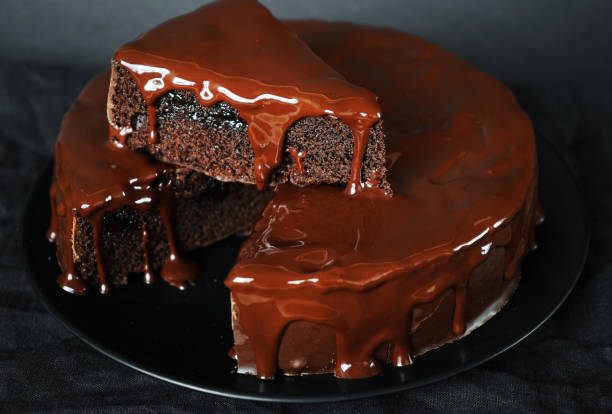 istock Chocolate cake with chocolate icing on a black plate next to a fork 2165404407