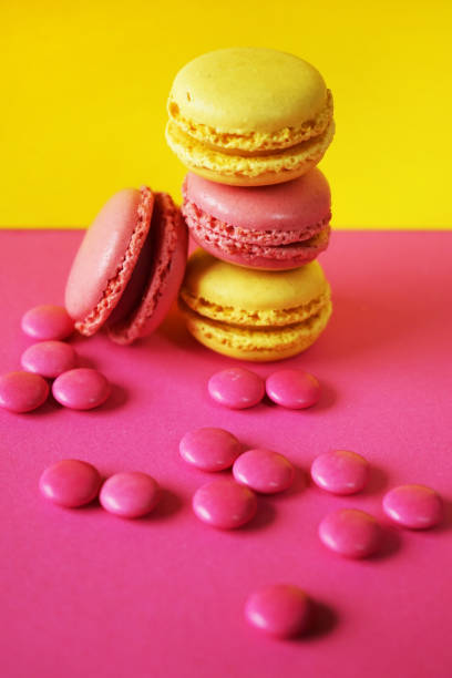 Pink and yellow macaroons next to scattered candies on a contrasting pink and yellow background