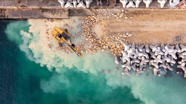 istock Waterfront construction site with excavator. Excavator working on a breakwater construction 2165408318